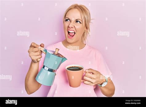 Une jeune femme blonde boit une tasse de café frais en colère et folle criant frustrée et