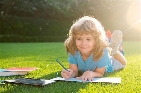 Lindo niño niño escribiendo notas en cuaderno al aire libre escuela