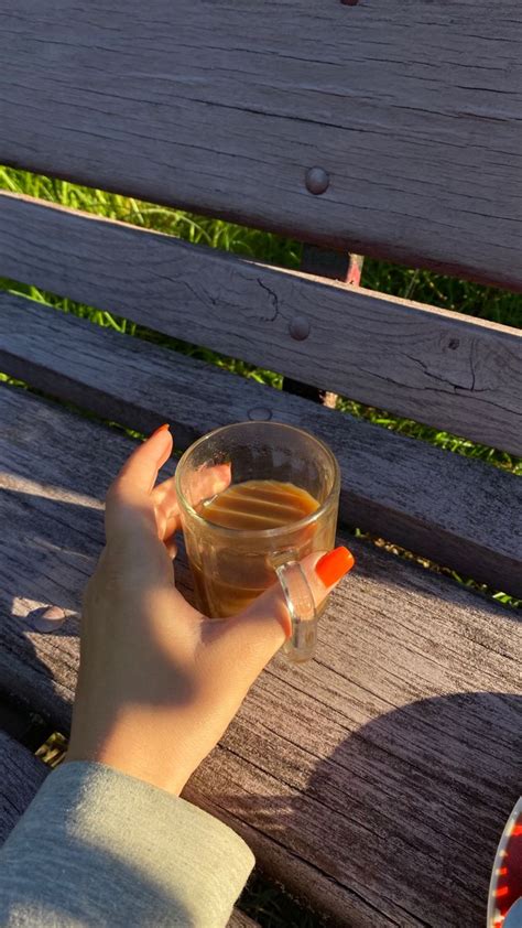 A Person Is Holding A Cup Of Tea On A Park Bench With Their Hand