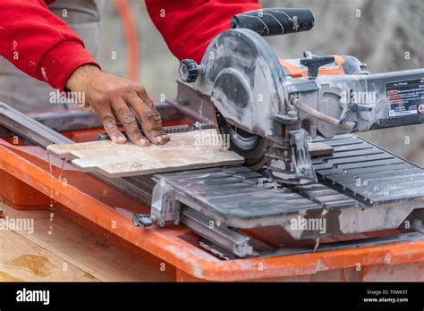 Worker Using Wet Tile Saw To Cut Wall Tile At Construction Site Stock