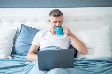 Premium Photo Cheerful Mature Man Working On Laptop In Bed With Coffee
