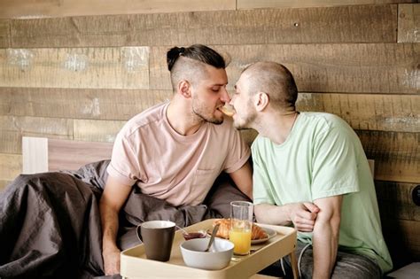 Joven Pareja Gay Enamorada Sentada En La Cama Y Comiendo Un Delicioso Croissant Juntos Foto