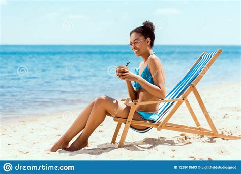 Happy African American Woman In Bikini And Sunglasses Drinking Cocktail In Coconut Shell While