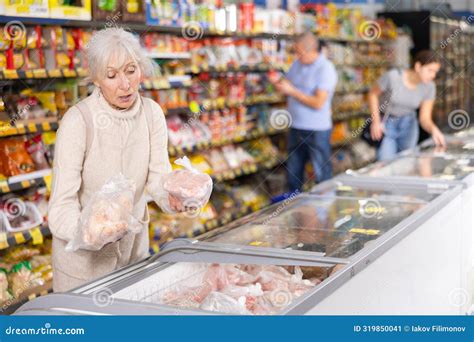 Elderly Woman Buyer Carefully Chooses Frozen Food In Grocery Store