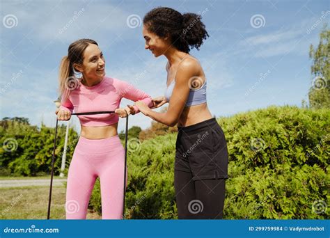 Two Smiling Women Doing Exercises With Resistance Band In Park Stock