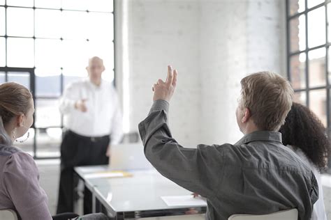 Male Employee Raising Hand For Asking Question At Conference In Office