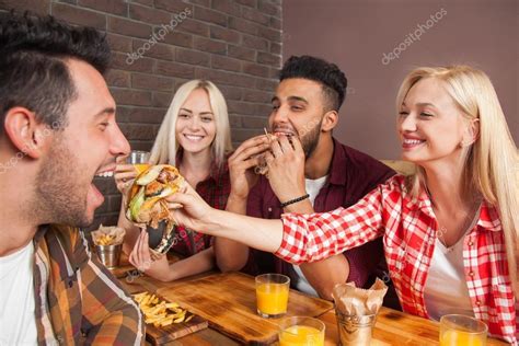 People Group Eating Fast Food Burgers Sitting At Wooden Table In Cafe