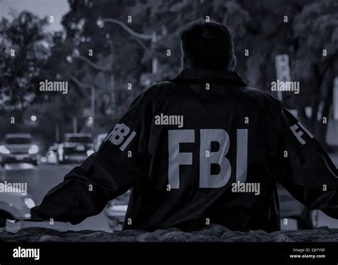 Male Fbi Agent Wearing Dark Blue Coat With Fbi Logo Looking Down The