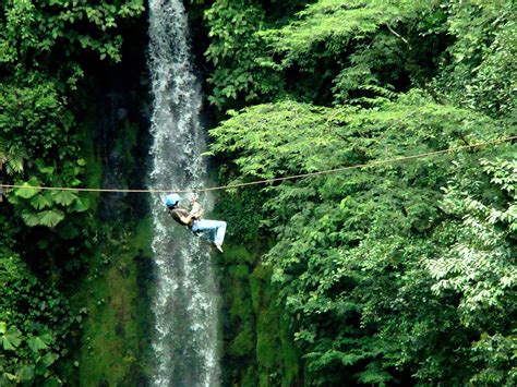 A Man Hanging From A Rope Above A Waterfall