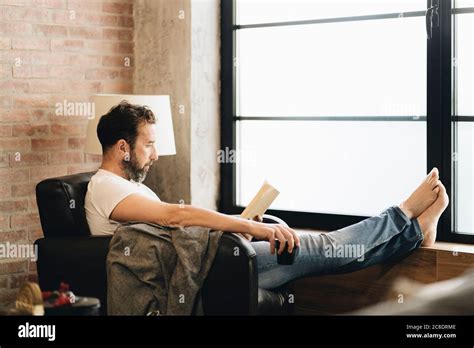 Mature Man Sitting Barefoot In Armchair Reading Bok Stock Photo Alamy
