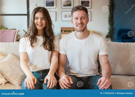 Young Couple Man And Woman Sitting On The Sofa Looking Happy Grimacing