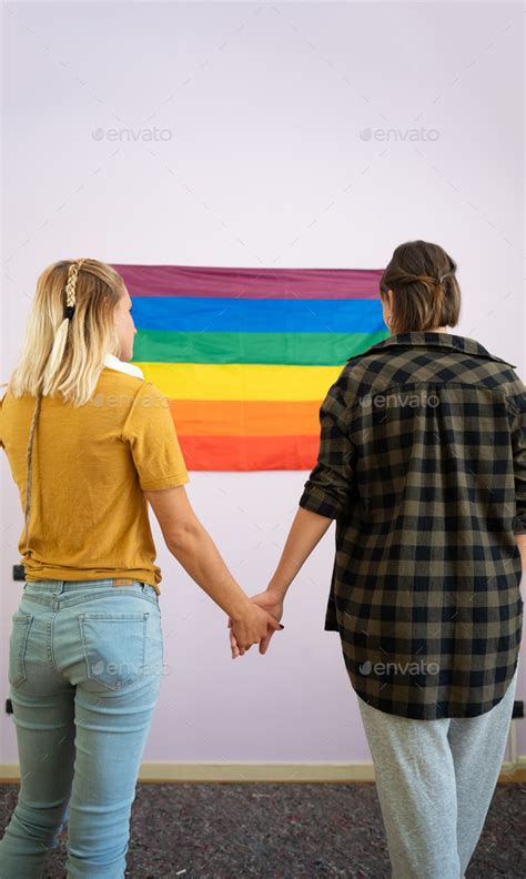 Two Proud Lesbian Women Holding Hands Gazing At The LGBT Symbol Of Love And Acceptance Stock