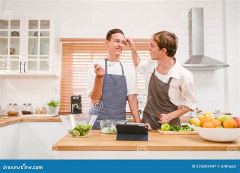 Portrait Of The Happy Caucasian Gay Couple Wearing Aprons Looking At Each Other With Smiles And
