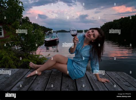 Young Brunette Woman Sitting On A Lakeside Dock At Sunset Enjoying A