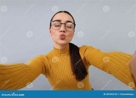 Young Woman Taking Selfie And Blowing Kiss On Grey Background Stock