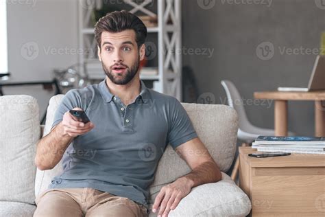 Shocking TV show. Handsome young man holding remote control and looking