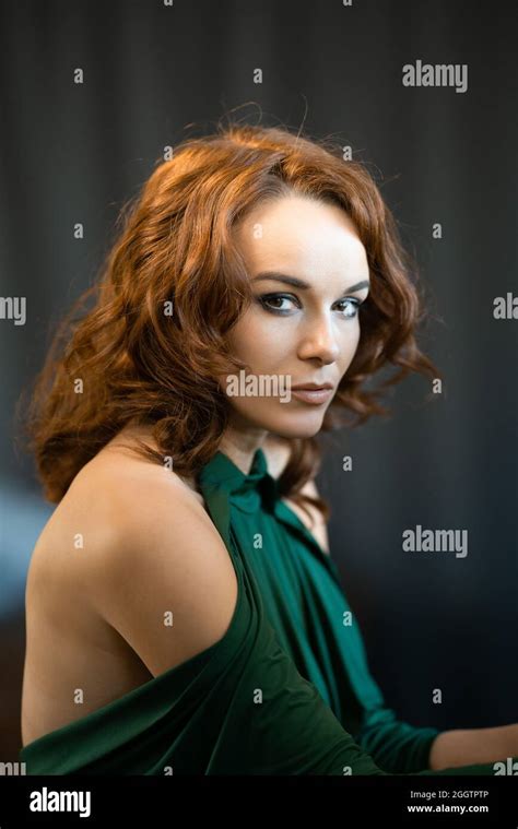 Portrait Of A Pretty Brunette Female In Green Drees Staring At The Camera On The Gray Background