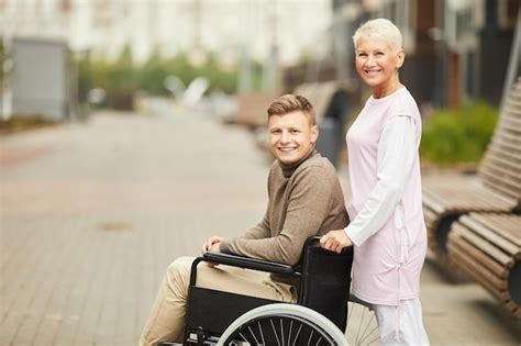 Infirmière blonde mature positive en uniforme poussant un fauteuil roulant avec un jeune patient