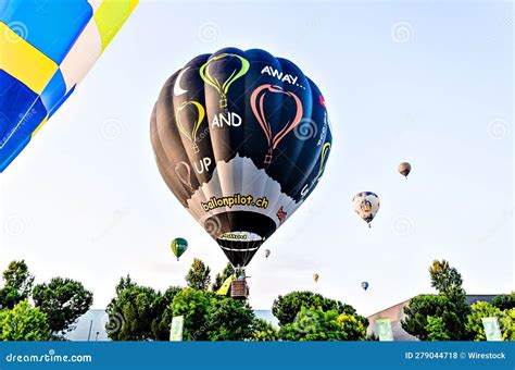 Group Of Vibrant Hot Air Balloons Soaring Above A Lush Row Of Evergreen