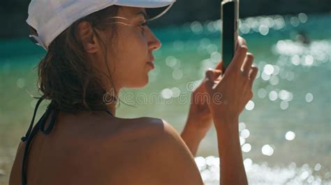 Close Up Rear View Tanned Woman Tourist In Bikini Sits On Sea Beach Close To Water Unlocks Her