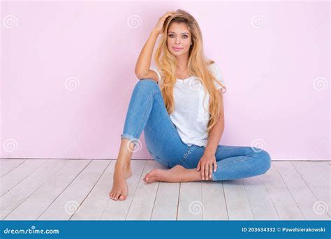 Beautiful Blonde Girl With Long Hair And Tanned Body Wearing White Shirt And Blue Jeans Stock