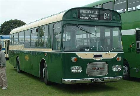 Two Green Buses Parked Next To Each Other On A Field With People