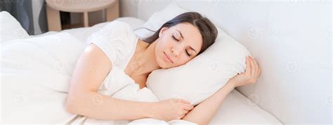 View An Attractive Young Woman Sleeping Well In Bed Hugging Soft White