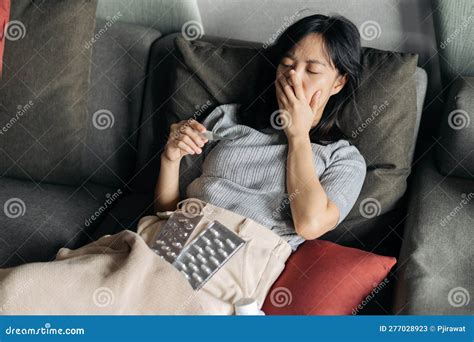 Sick Asian Woman Reading Clinical Thermometer While Cough On A Sofa Bed