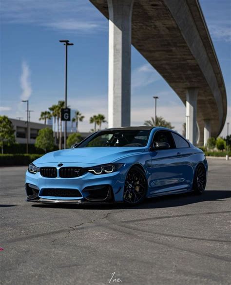 a blue bmw is parked in front of a large building with an overpass above it