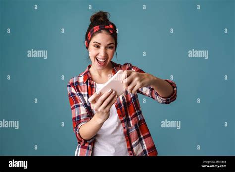 Excitée belle fille de brunette jouant en ligne jeu sur le téléphone mobile isolé sur fond bleu