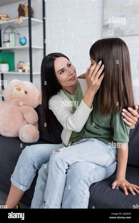 Happy Brunette Babysitter Looking At Girl While Sitting On Couch Stock Photo Alamy