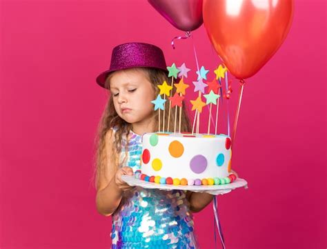 Déçu petite fille blonde avec chapeau de fête violet tenant des ballons d hélium et regardant