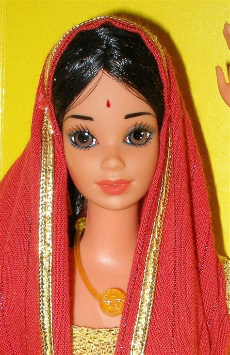 A Doll Wearing A Red And Gold Sari With An Orange Head Piece On Its Head