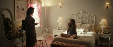 two women sitting on a bed talking to each other in a room with pink carpet