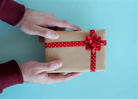 Las Manos De Los Hombres Sostienen Un Regalo Con Un Lazo Rojo Y Una