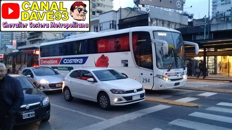 A White Bus Driving Down A Street Next To Tall Buildings And People