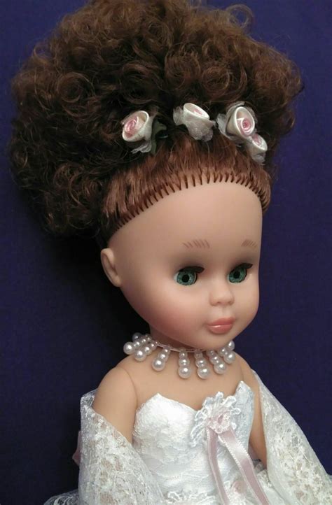 A Doll With Curly Hair Wearing A White Dress And Pearls On It S Head