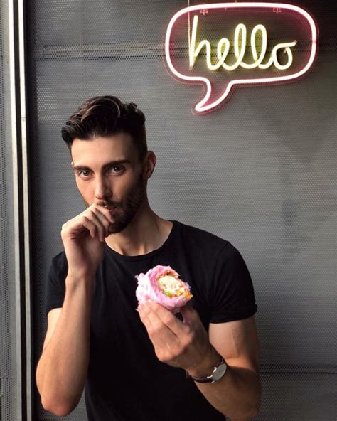 A Man Holding A Pastry In Front Of A Neon Sign With The Word Hello On It