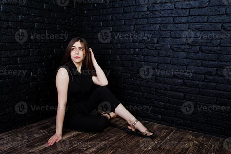 Portrait Of A Beautiful Brunette Girl In Black Jumpsuit Sitting And Posing In The Studio