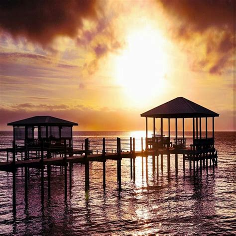 The Sun Is Setting Over The Water And Some Piers Are In The Foreground