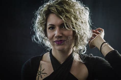 Backlit Portrait Of A Curly Blonde Woman Who Is Adjusting The Hair Behind Her Head Stock Image
