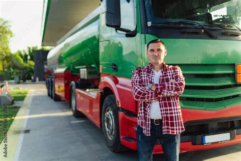 a male tanker or truck driver poses next to his vehicle at a gas ...