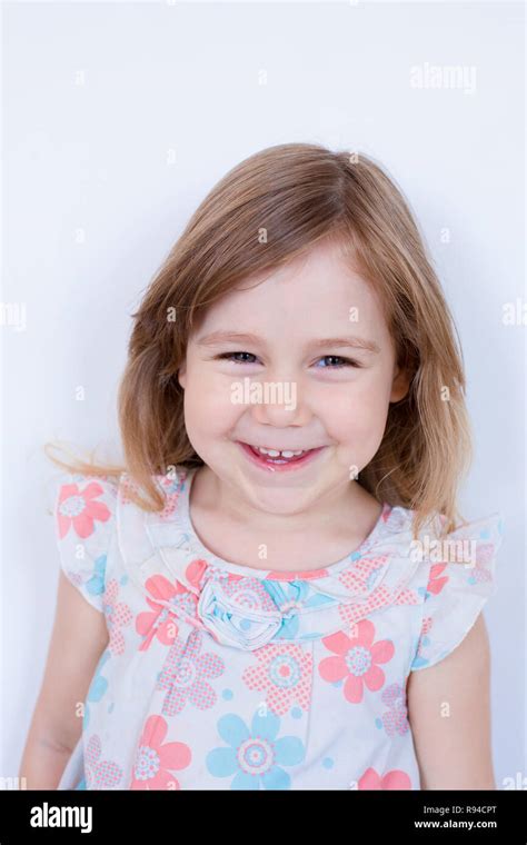Portrait Of Three Years Old Blonde Girl With White Dress With Red And Blue Flowers Looking And
