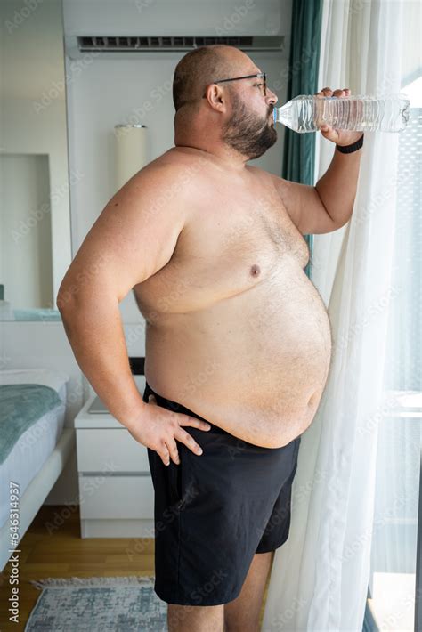 Excess Weight Man Drinking Water In Air Conditioned Hotel Room Looking