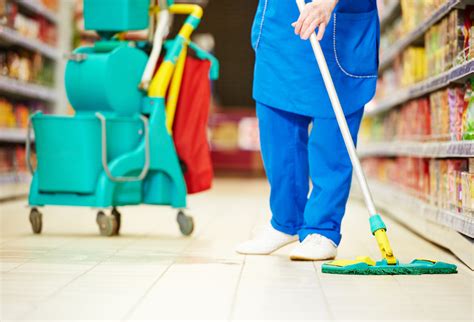 Female Cleaner Worker In Uniform With Mop Cleaning The Floor Of