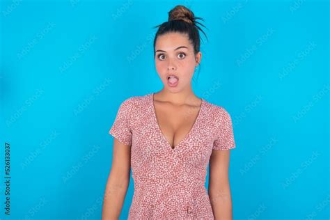 Shocked Beautiful Brunette Woman Wearing Floral Dress Over Blue Background Stares Bugged Eyes