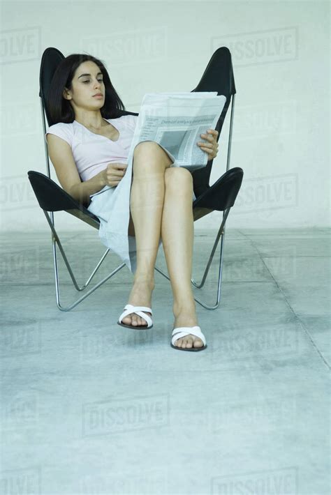 Young Woman Sitting In Chair With Legs Crossed Reading Newspaper Full