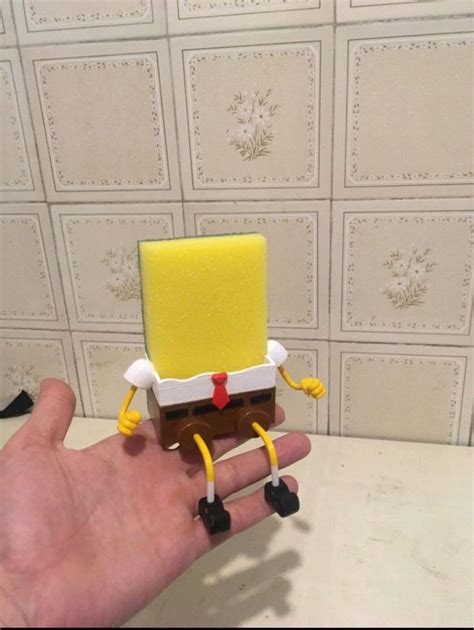 A Hand Is Holding A Spongebob Toy In Front Of A Wall With White Tiles