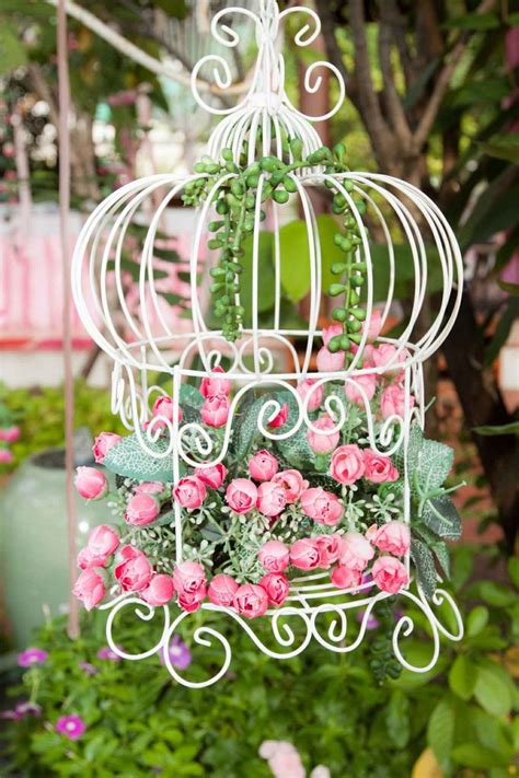 A White Birdcage With Pink Roses Hanging From It S Sides In A Garden