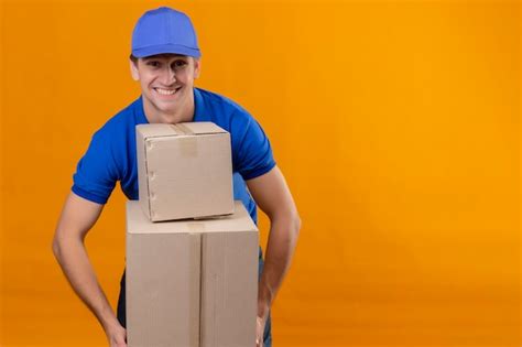 Jovem bonito entregador de uniforme azul e boné segurando caixas de